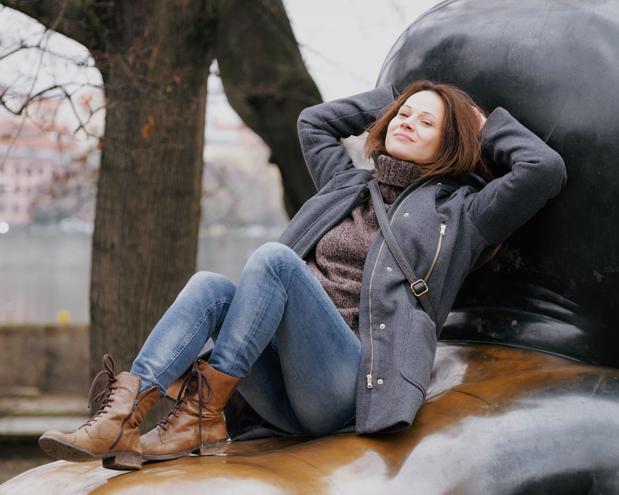 Femme portant un manteau gris, un pull à col roulé, un jean et des bottines marron en extérieur.
